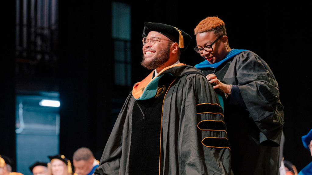 UNCG Dr. Tiffanie Lewis-Durham places the doctoral hood on one of her students